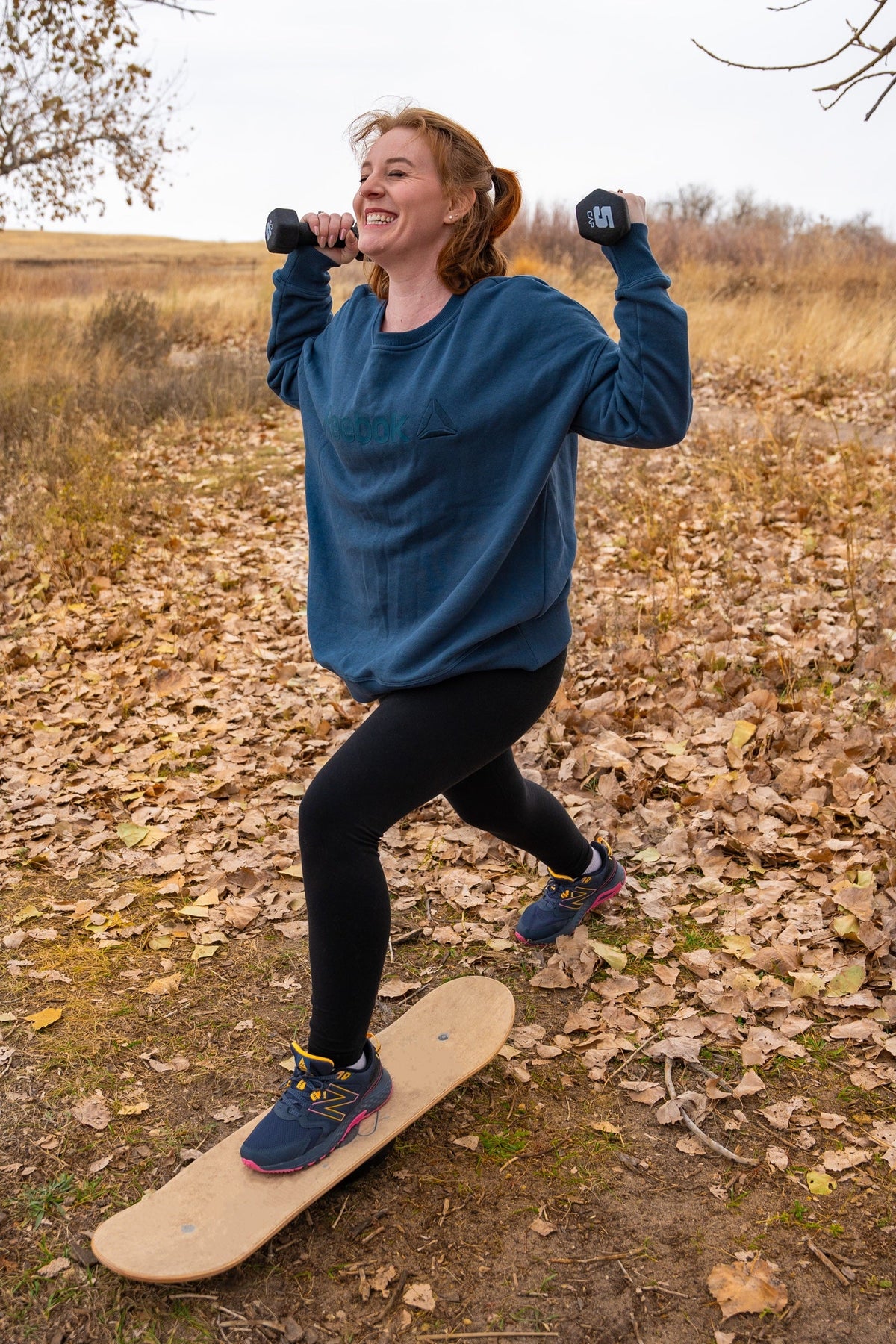 Woman doing a lunge with dumbbells on a Whirly Board in autumn leaves