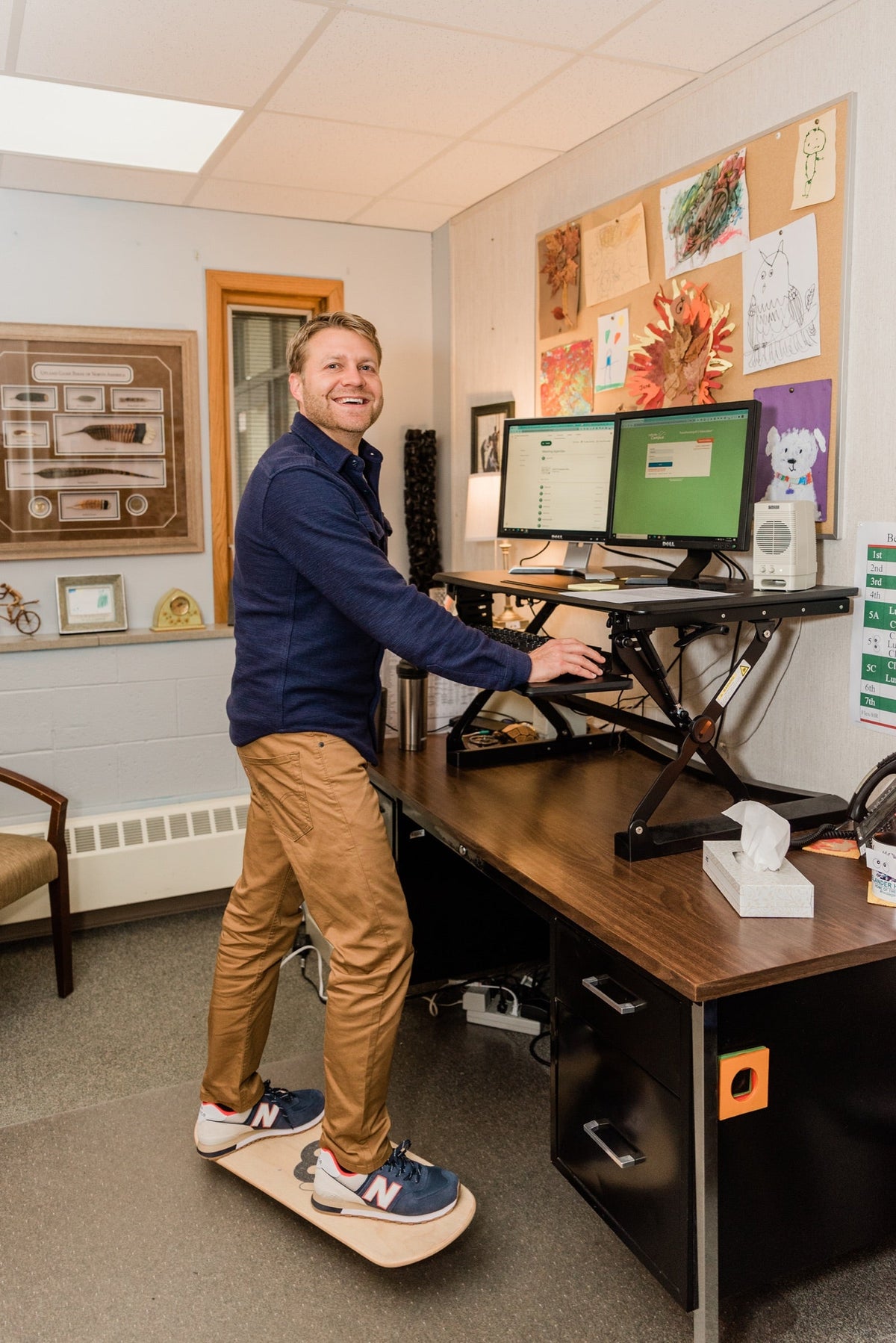Smiling man working at a standing desk while balancing on a Whirly Board