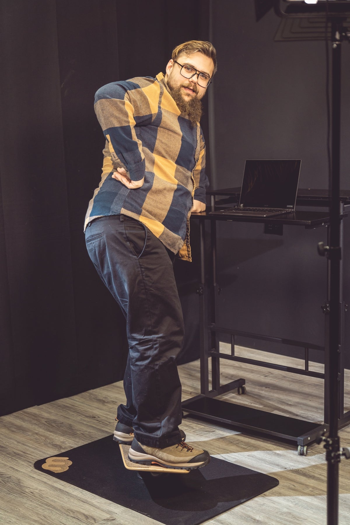 A man strikes a superhero pose on a Whirly Board Desk Rider at his standing desk