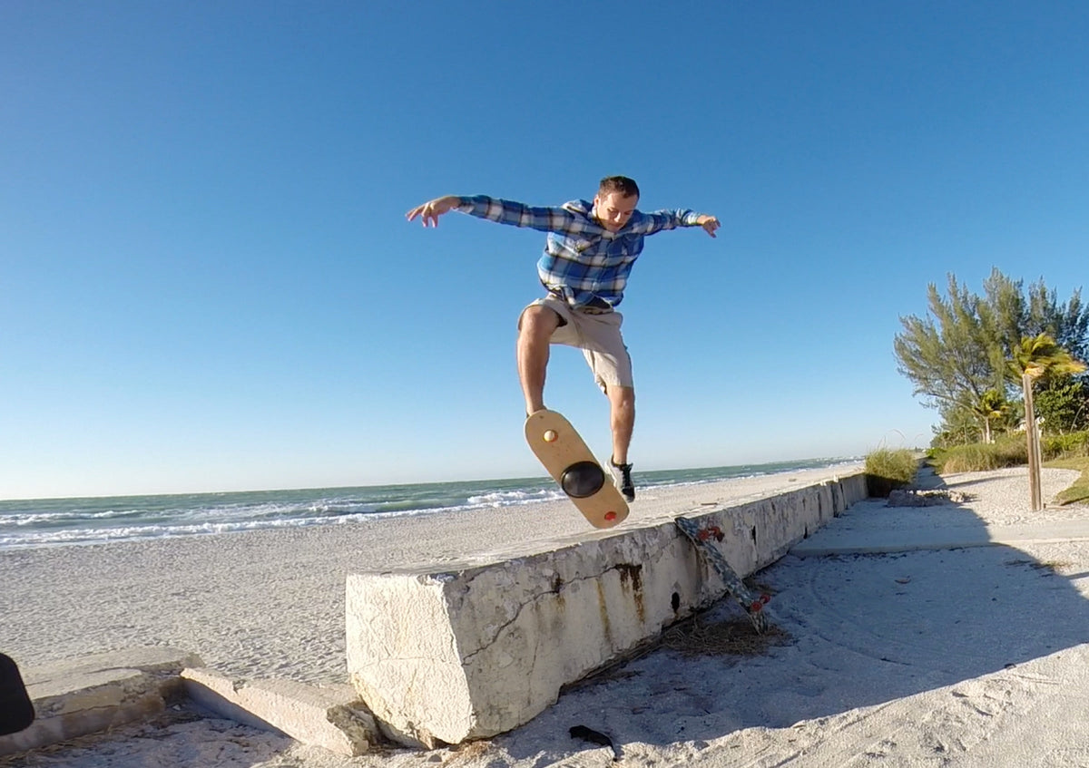 Man jumping a Whirly Board off a concrete ledge at the beach