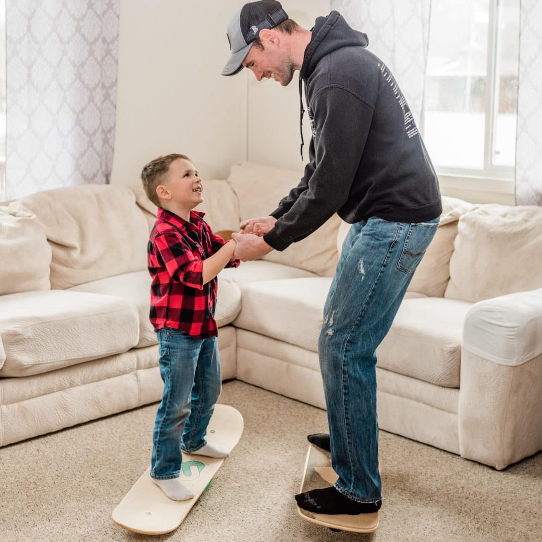 Dad holding his son's hands as they both balance on Whirly Board balance boards in the living room