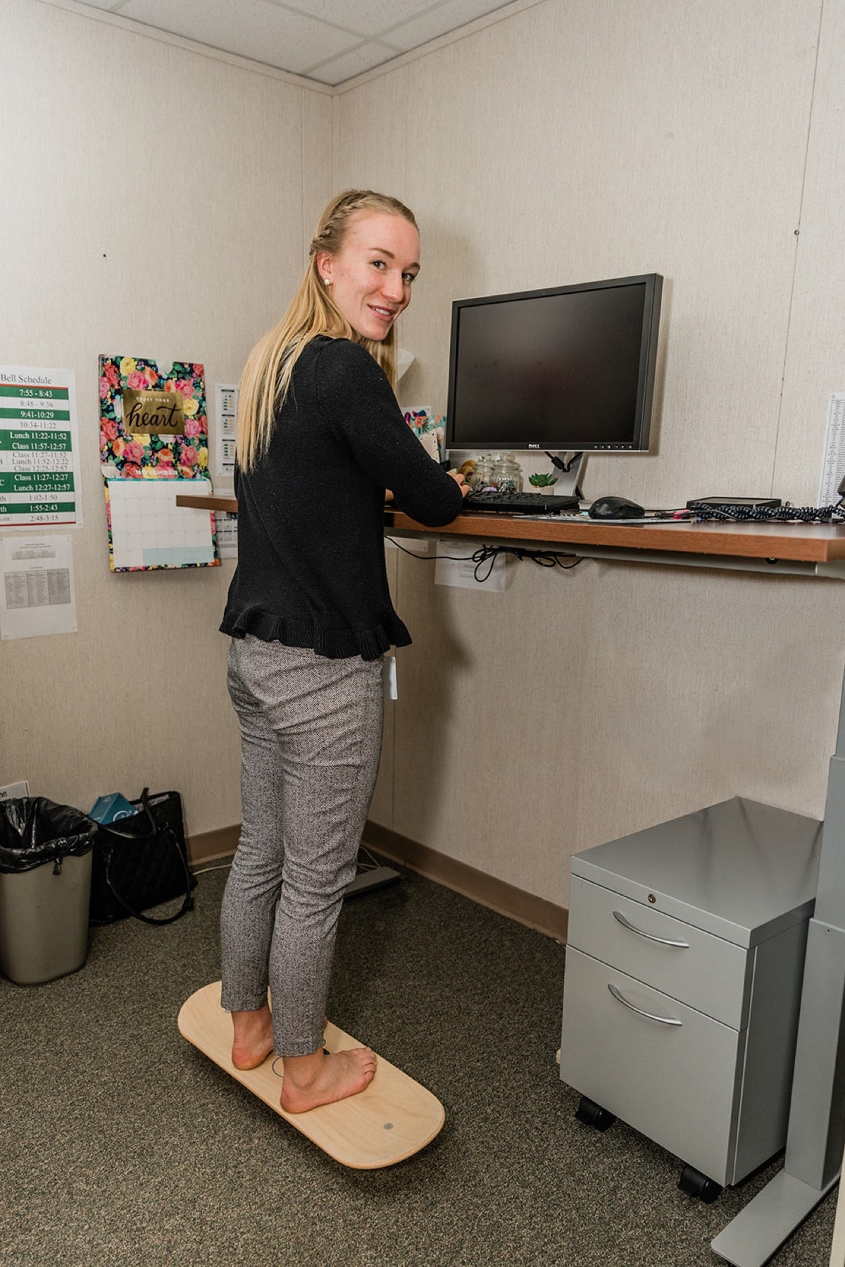 A woman smiling at her standing desk while balancing on a Whirly Board