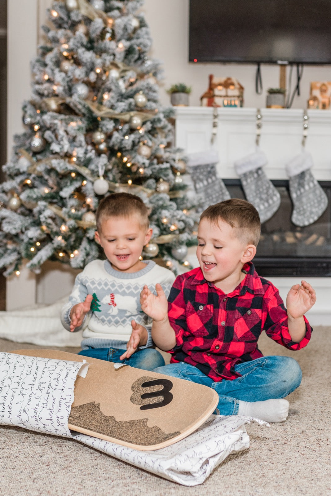 Two brothers laugh by the Christmas tree as they unwrap a Whirly Sport 360