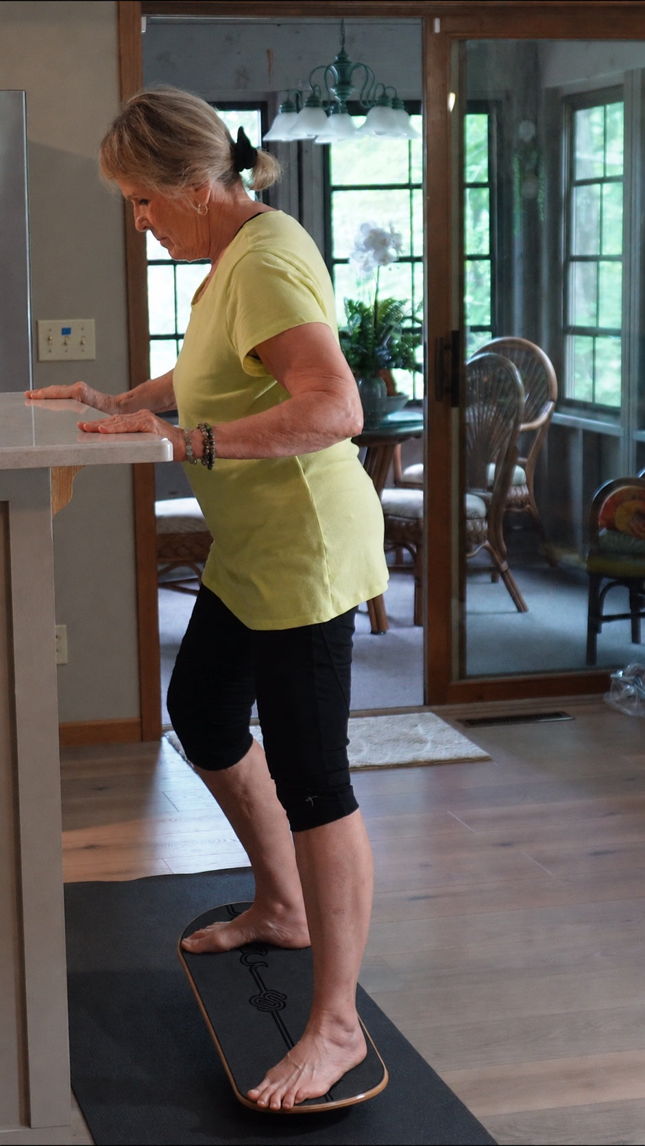 A woman stands on the Whirly Complete deck at her kitchen counter with both hands resting on the countertop