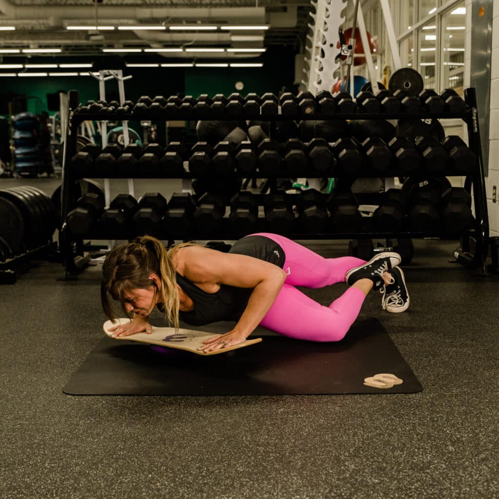 Woman performs plank exercise on fitness balance board.