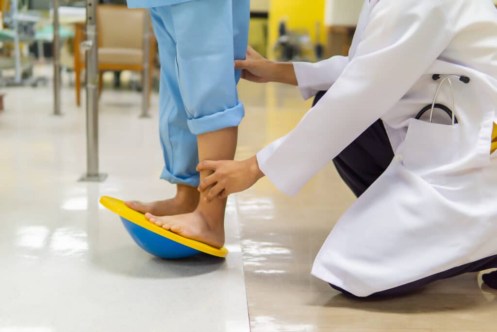 Doctor checks patient's ankle on a wobble board.